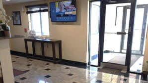 A reception area with a marble floor, a reception desk, a television screen, and a glass door leading outside. - Eco-Lux Inn (Norfolk)