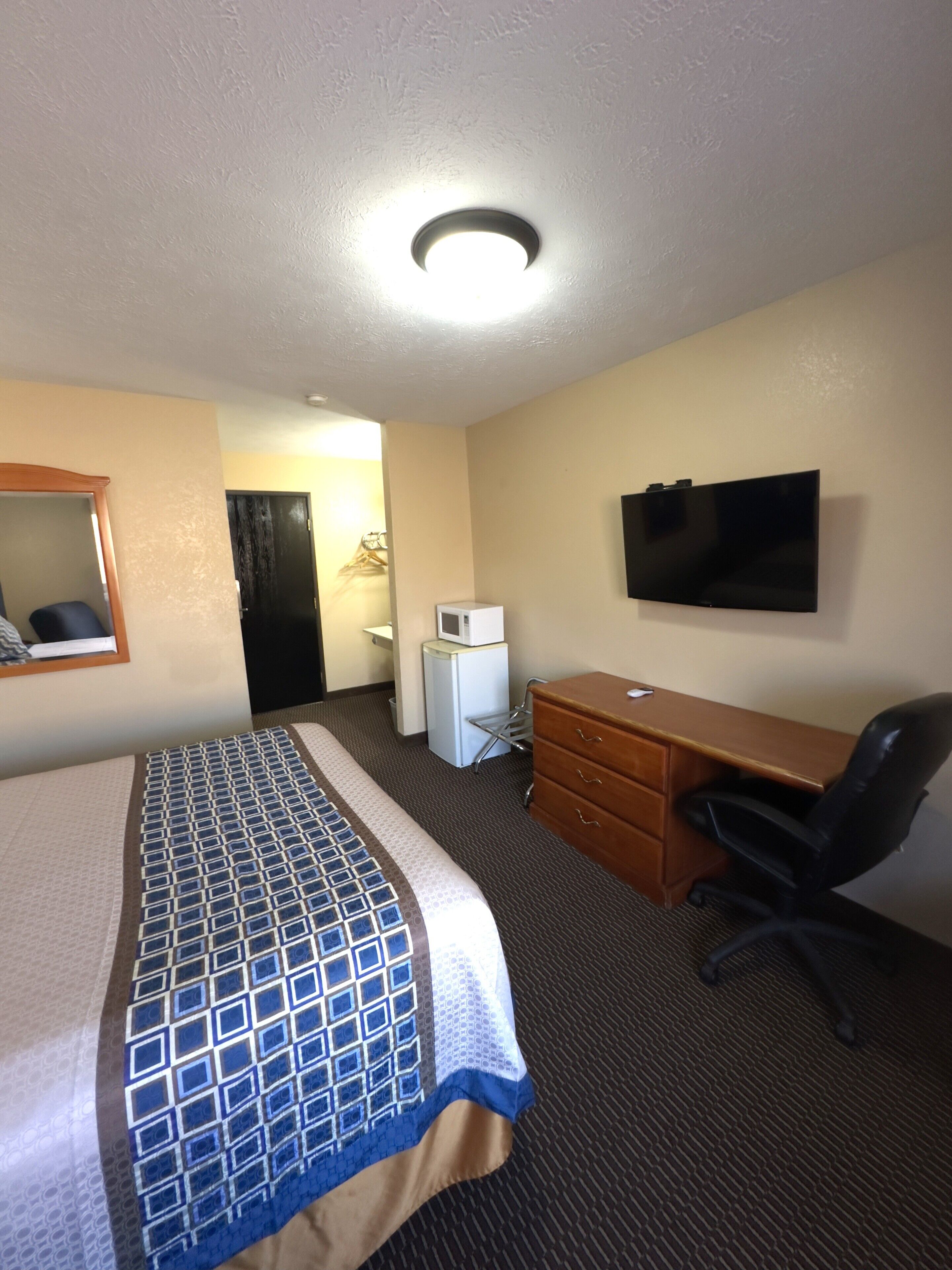 A hotel room with a bed, a desk, a chair, a television, and a microwave.