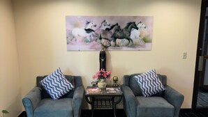 A reception area with two grey sofas, a small table with a vase of flowers, and a painting of horses on the wall. - Eco-Lux Inn (Norfolk)