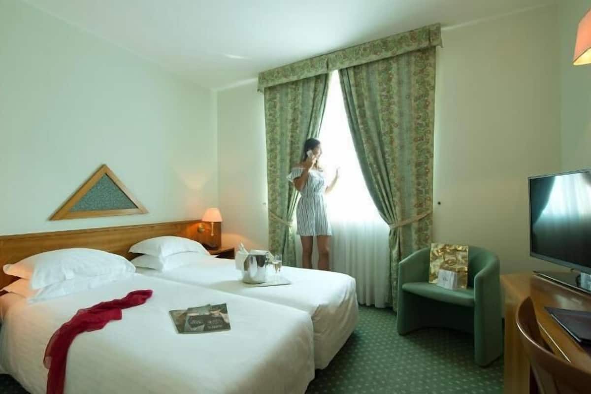 A hotel room with two beds, a television, a desk, and a window with curtains.