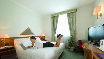 Una habitación de hotel con una cama, un escritorio con una computadora portátil, un televisor y una planta en maceta.