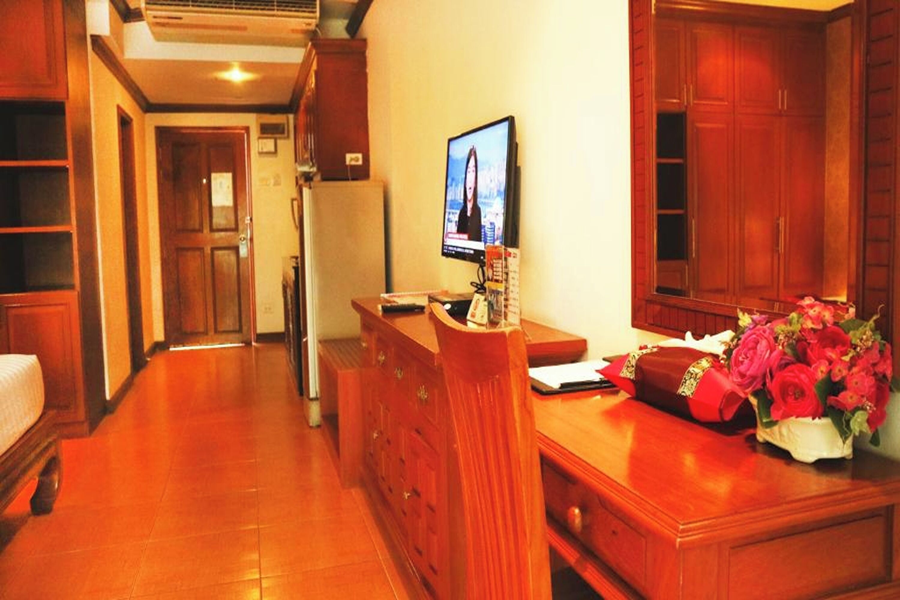 A hotel room with a wooden desk, a television, and a bouquet of flowers.