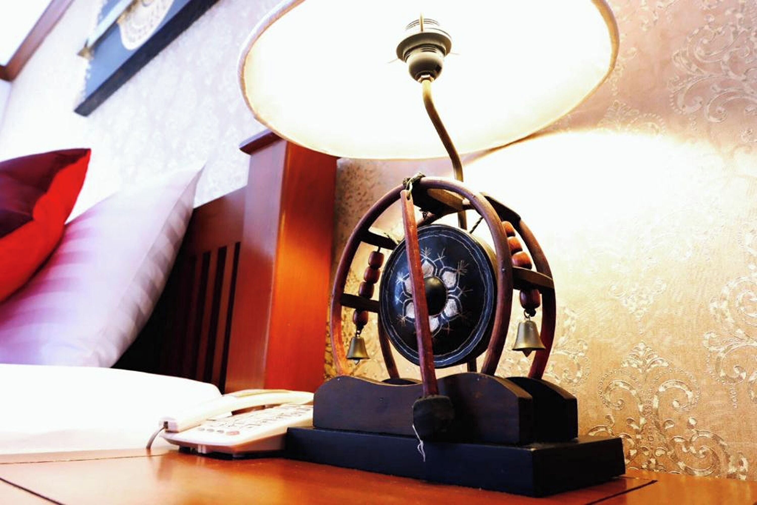 A vintage-style desk lamp with a classic design, a telephone, and a lamp on a wooden surface in a room with patterned wallpaper.