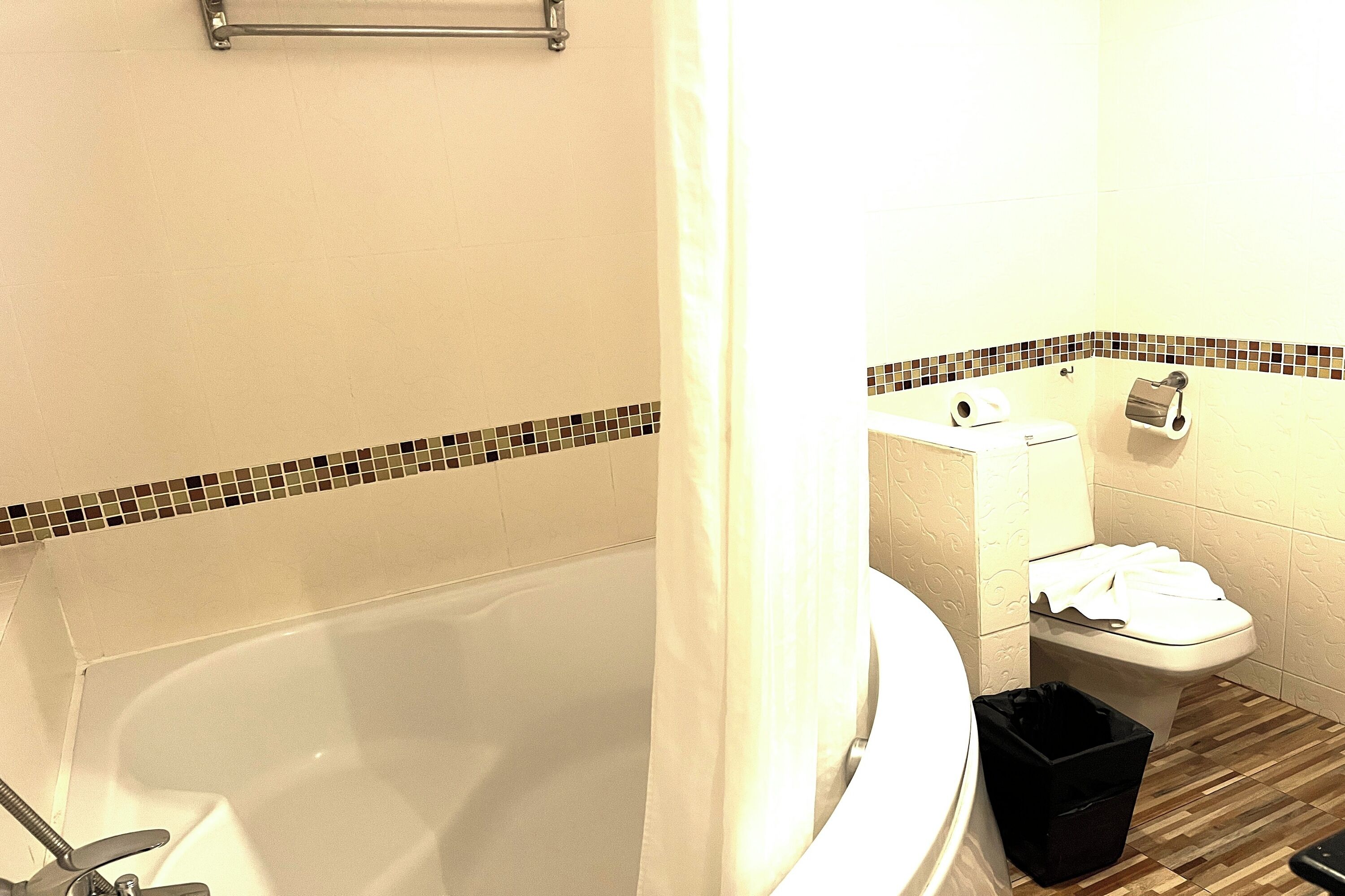 A bathroom with a bathtub, toilet, and a trash bin.