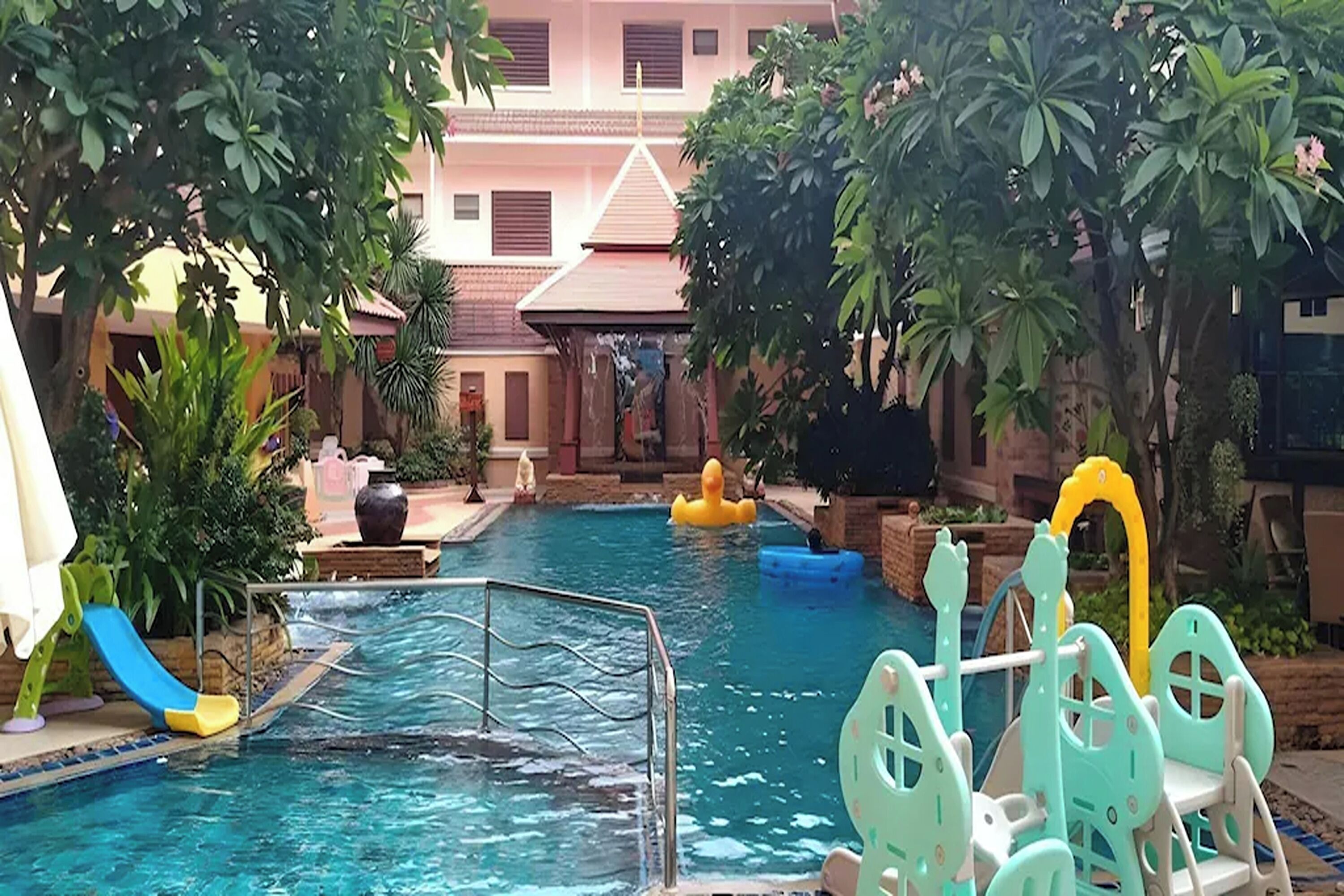 An indoor swimming pool with a slide, inflatable toys, and a poolside area with plants.