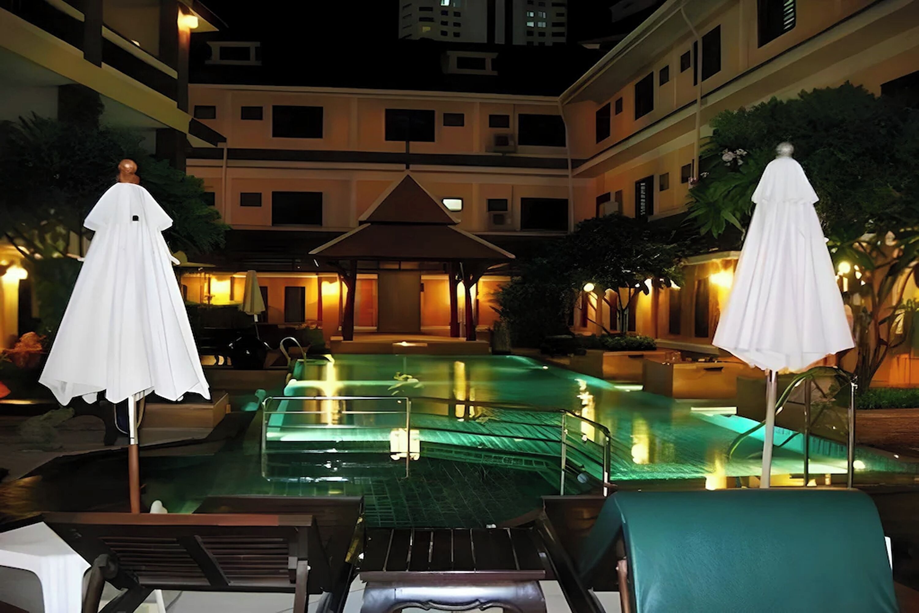 A swimming pool with lounge chairs and umbrellas, surrounded by a building with multiple floors and balconies.