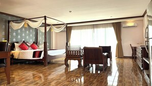 A hotel room with a four-poster bed, a wooden chair, a desk, and a dresser. - Aiyaree Place Hotel (Pattaya)