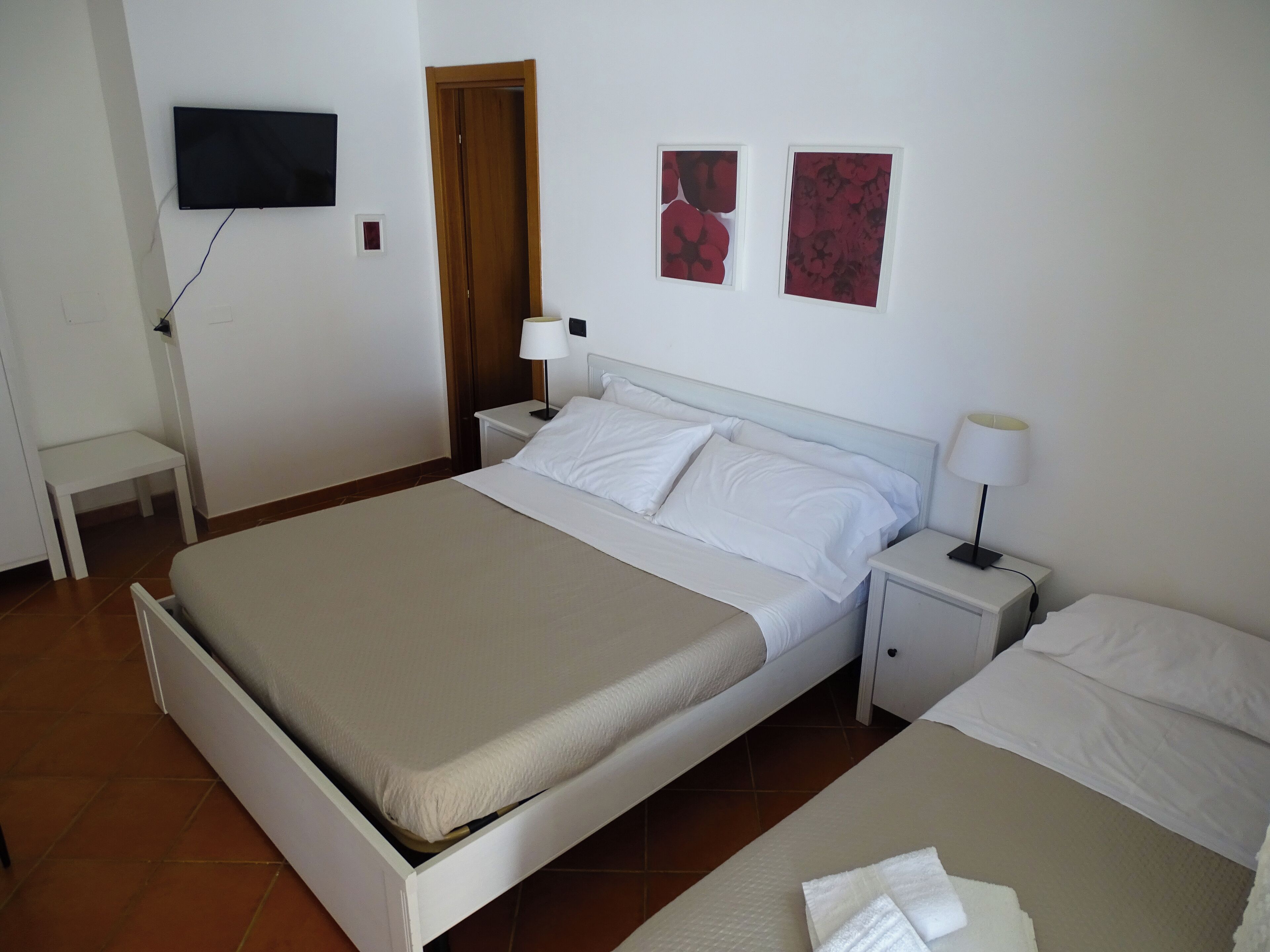 A hotel room with a bed, bedside tables, a TV mounted on the wall, and two framed pictures.