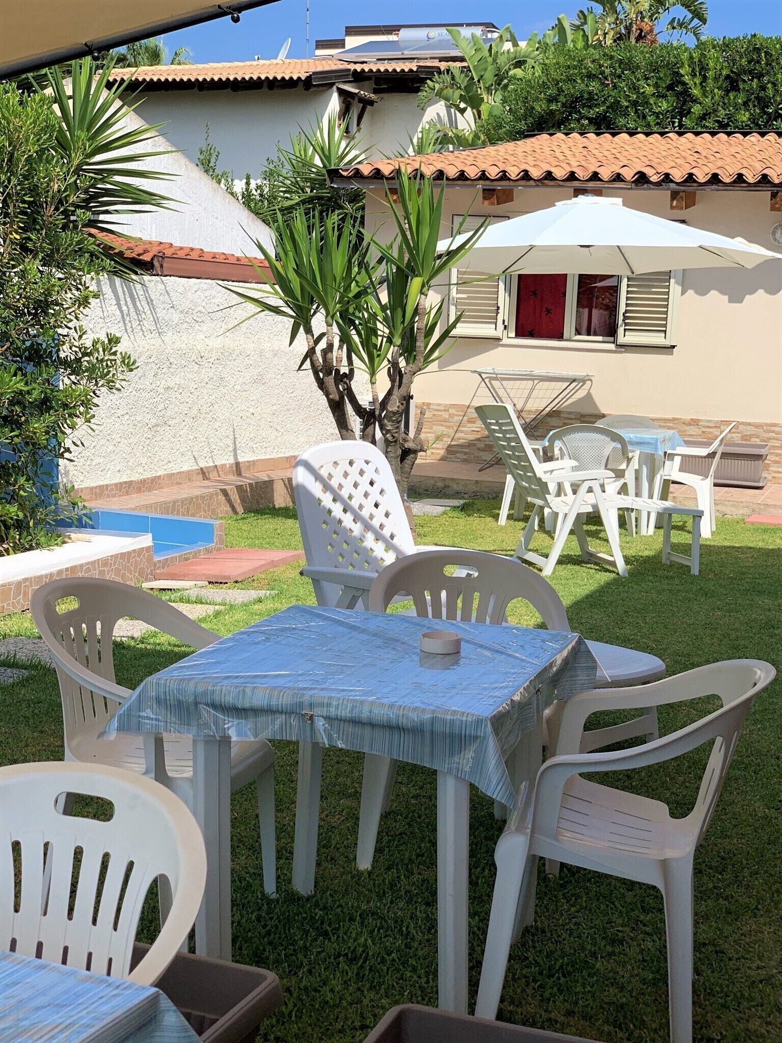 Een terras met een tafel en stoelen, een kleine boom en een gebouw met pannendak op de achtergrond.