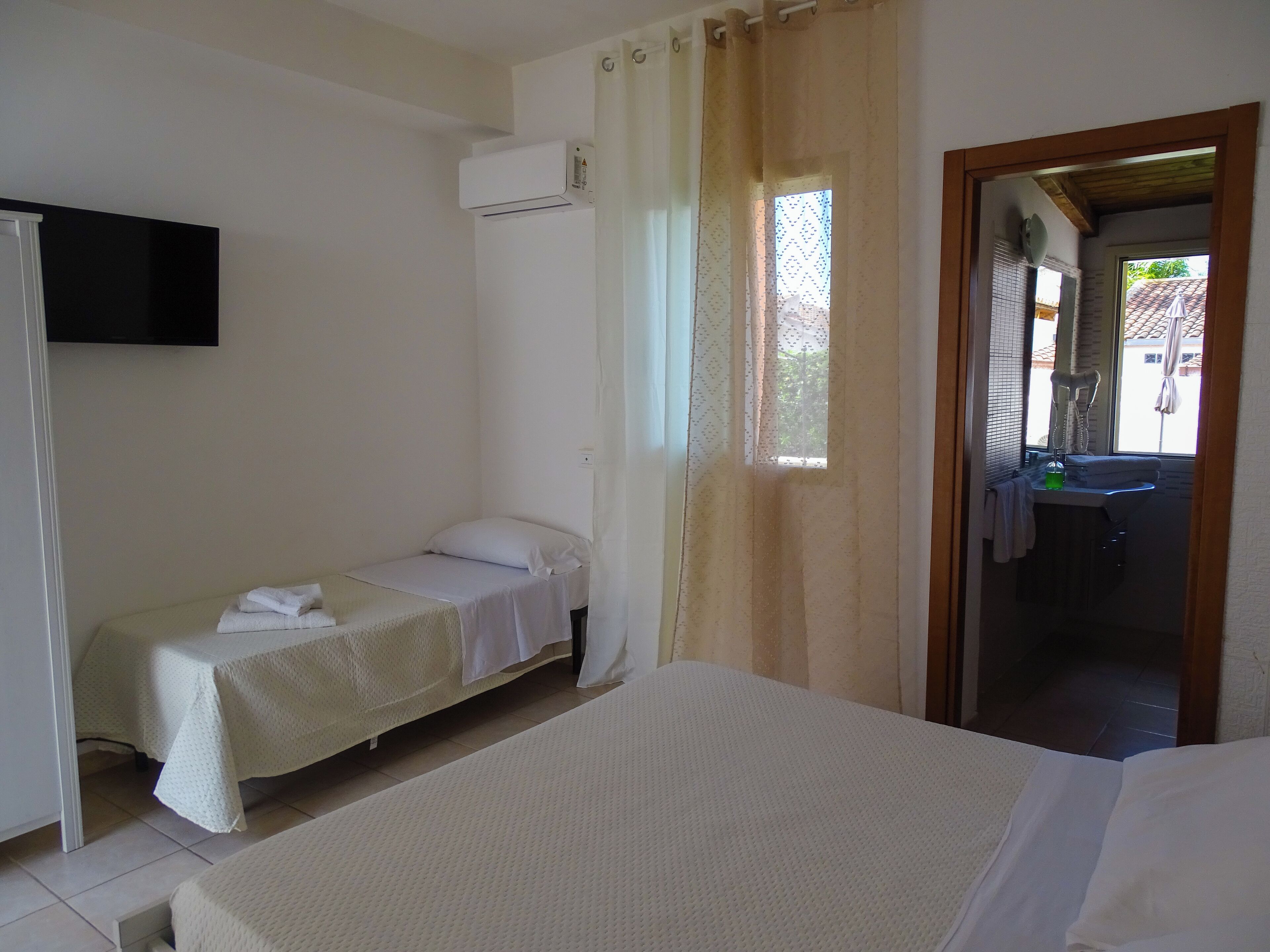 A room with a bed, a small bedside table, a window with curtains, and an air conditioning unit.