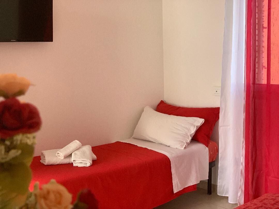 Una camera piccola con un letto singolo, cuscini bianchi e una coperta rossa.