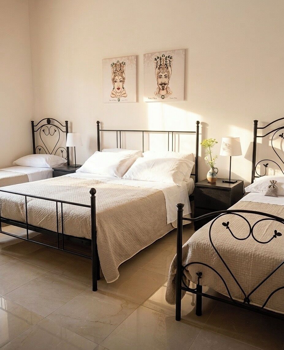 A bedroom with two beds, each with a black metal frame, white bedding, and a nightstand with a lamp. There are two framed pictures on the wall above the beds.