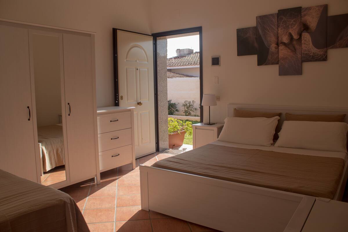A bedroom with a bed, a wardrobe, a nightstand, and a window with a view of the outside.