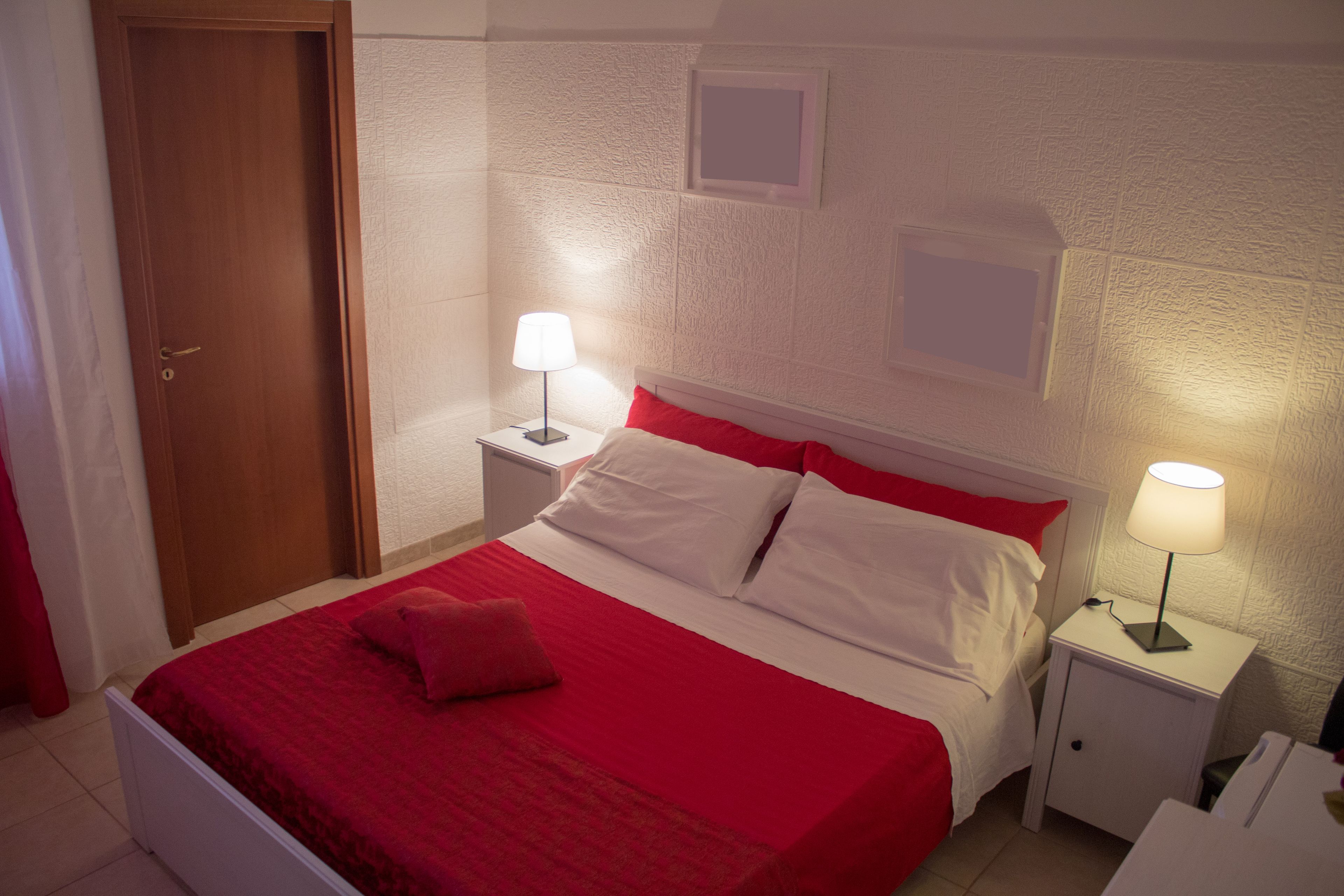 Una cama bien hecha con ropa de cama roja, un cabecero blanco y dos mesitas de noche con lámparas.