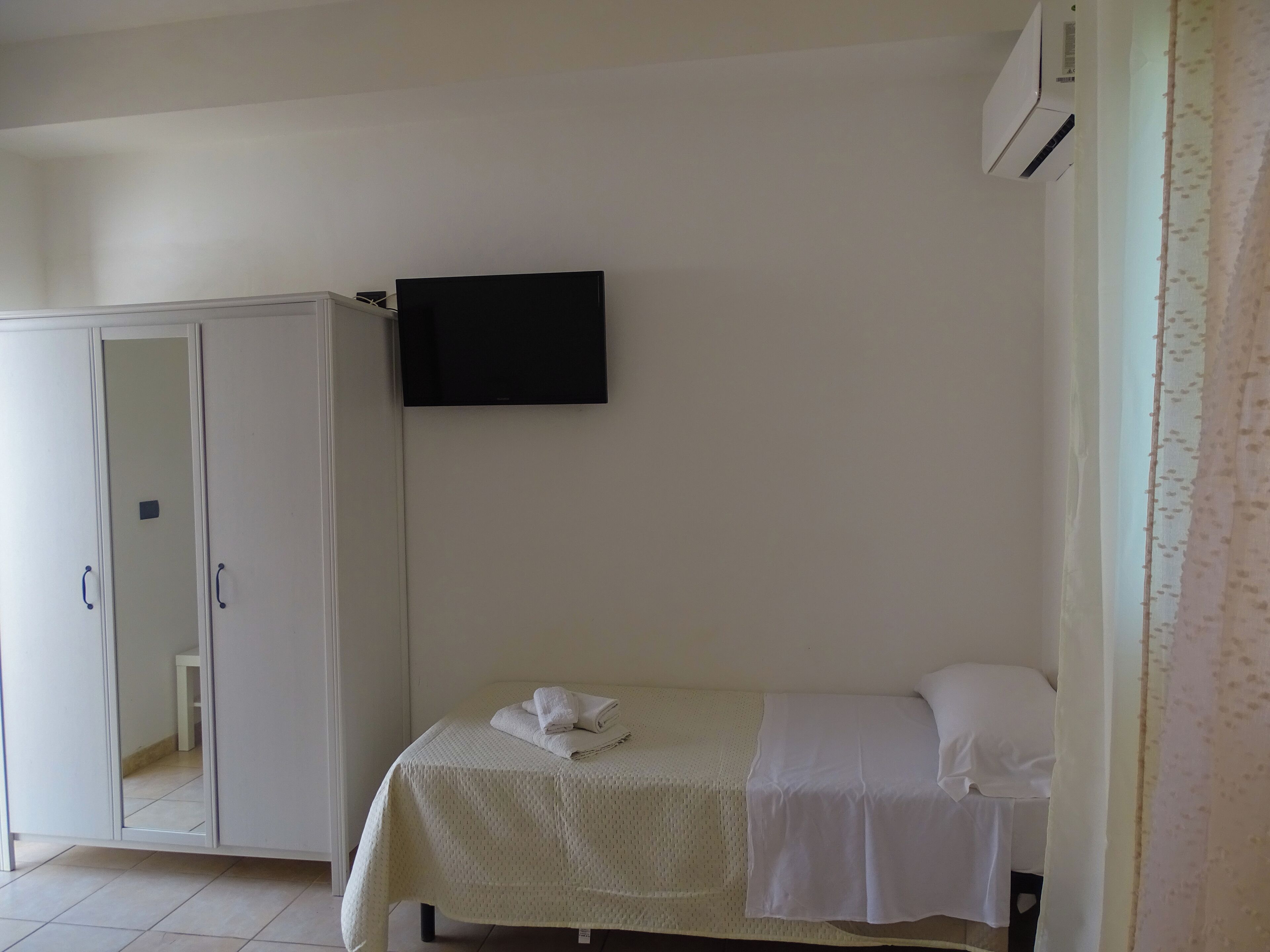 A room with a bed, a wardrobe, and a flat-screen TV mounted on the wall.