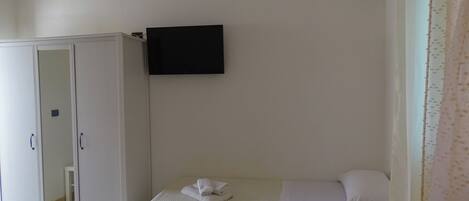 A room with a bed, a wardrobe, and a flat-screen TV mounted on the wall.