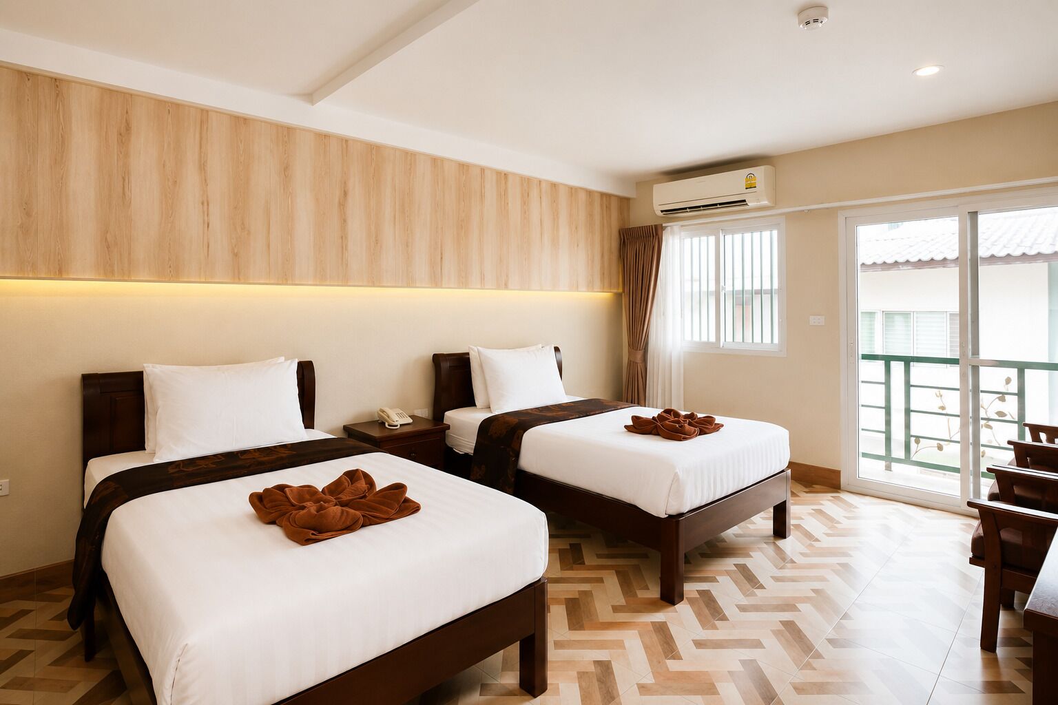 Une chambre d’hôtel avec deux lits, une tête de lit en bois, un appareil de climatisation, un téléphone et une vue sur l’extérieur.