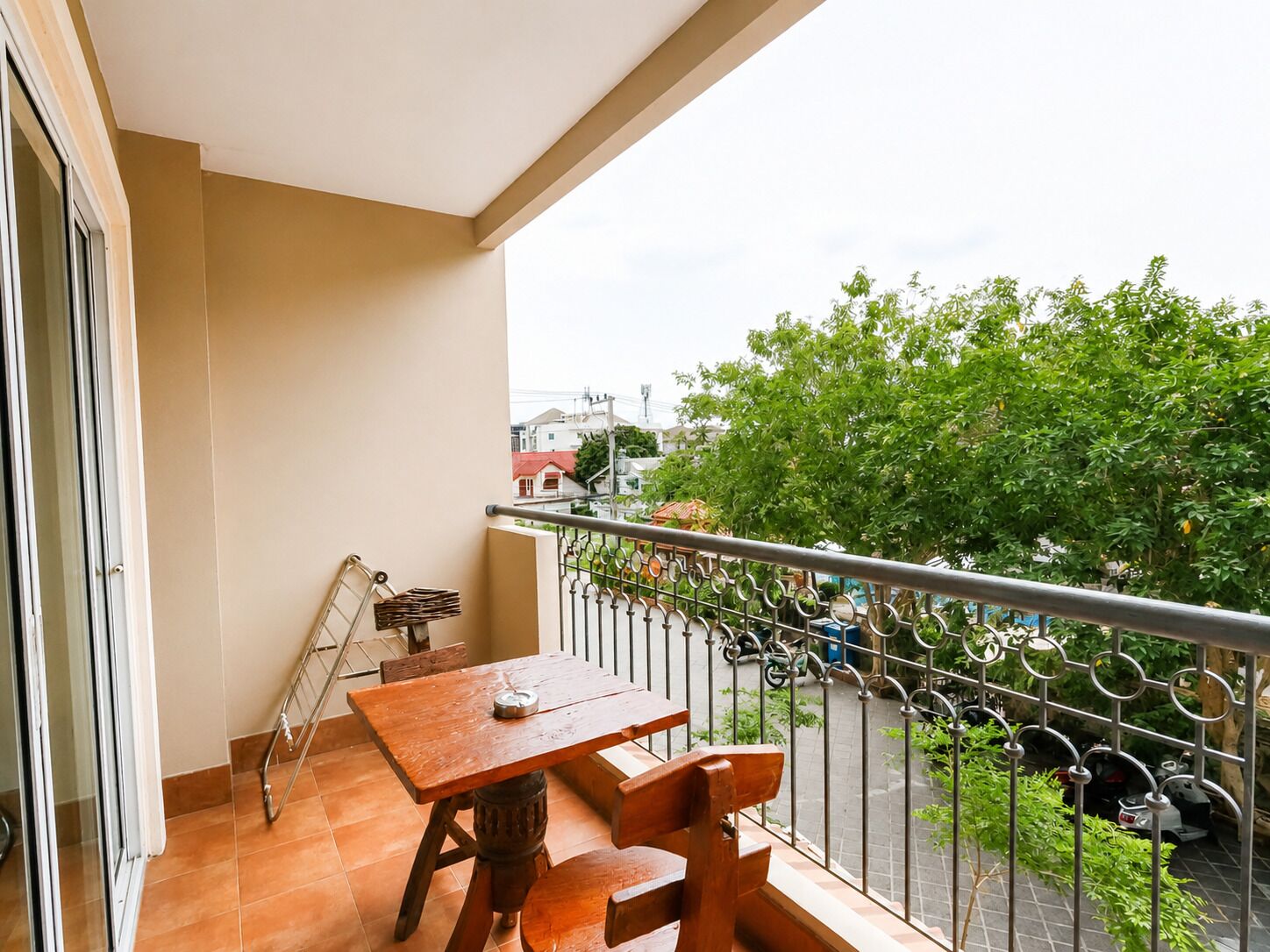 Un balcone con tavolo e sedie, una ringhiera in metallo e vista su una strada con motociclette parcheggiate e alberi.