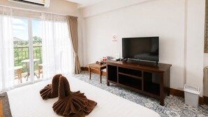 A hotel room with a bed, a television, a desk, and a balcony with outdoor seating. - Harmony Inn (Pattaya)