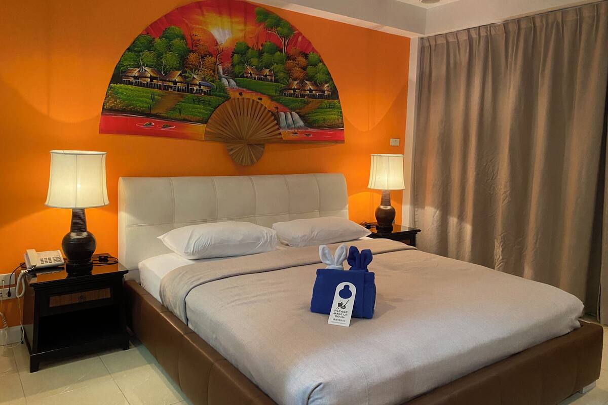 A hotel room with a large bed, two bedside lamps, a painting on the wall, and a curtain.