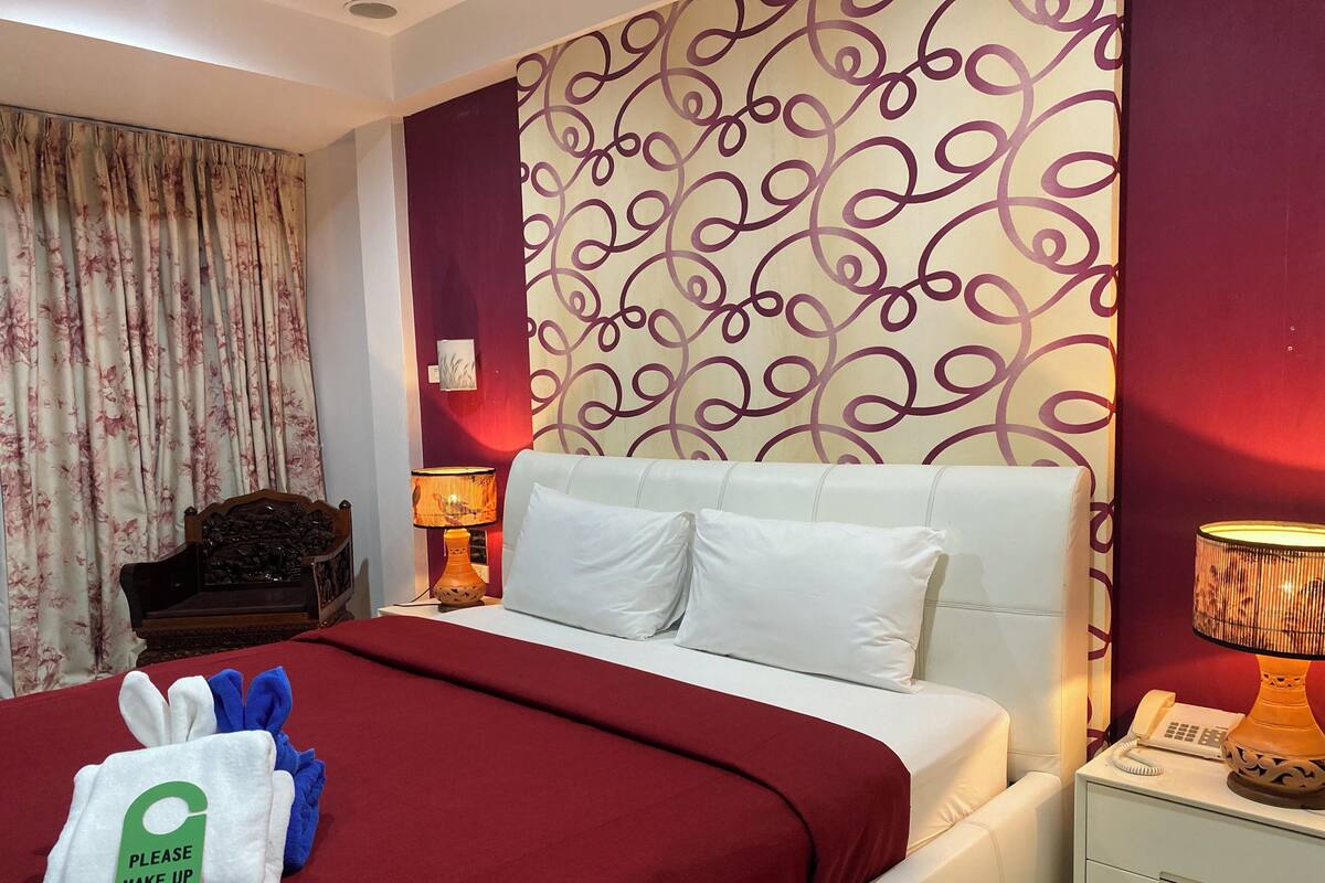 A hotel room with a bed, a nightstand, a lamp, a chair, and a sign indicating the room is ready for guests.