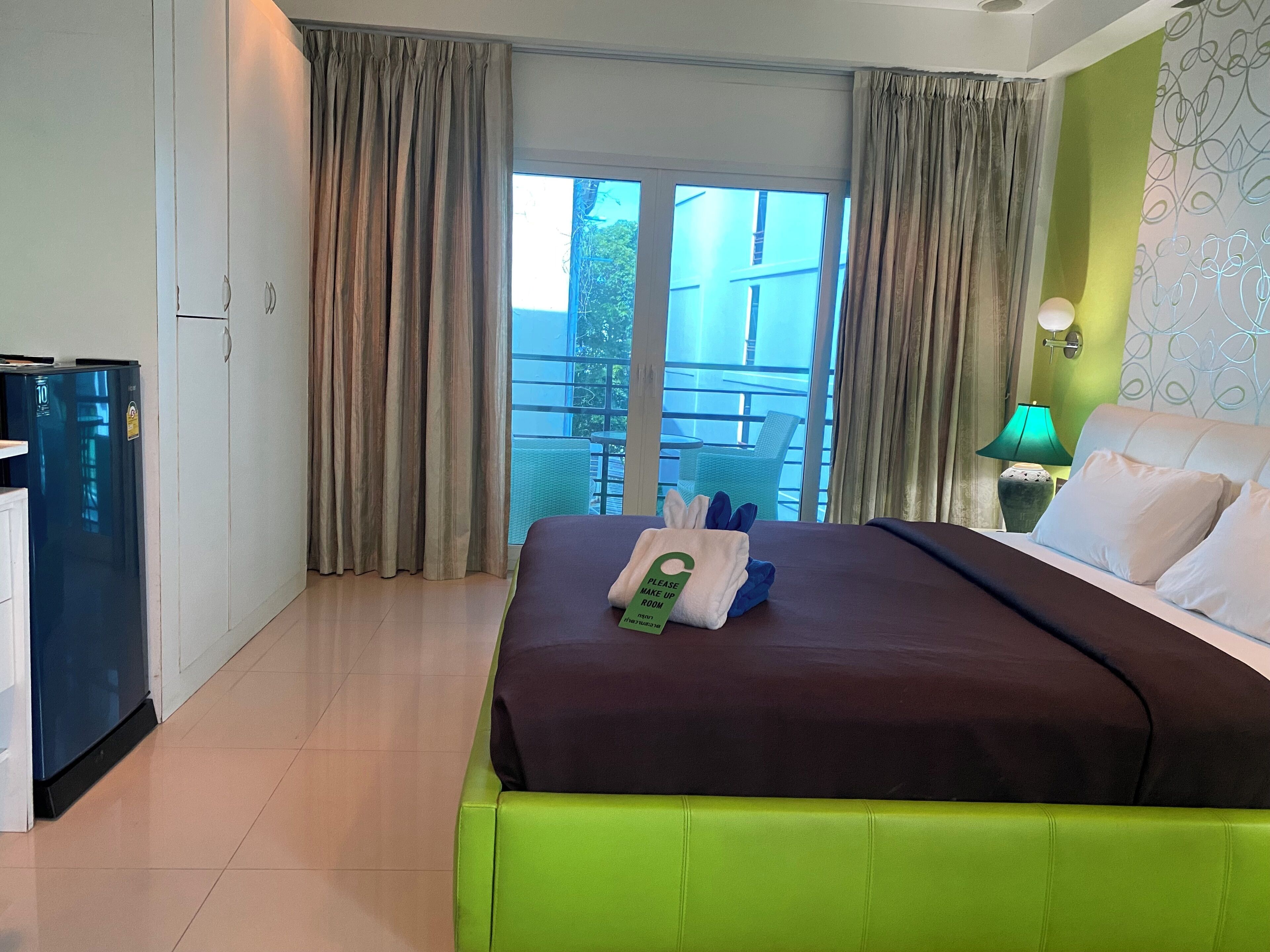 A hotel room with a bed, a desk, a refrigerator, and a balcony with a chair.