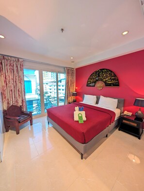 A hotel room with a bed, a nightstand, a chair, a large window, and a red wall.