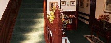 Een trap met een tapijtvloer die leidt naar een kamer met een boekenkast en een bloemenvaas.