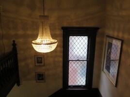 Een kroonluchter hangt aan het plafond, een raam met een rasterpatroon en twee ingelijste foto's aan de muur.