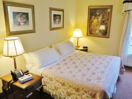 Habitación de hotel con cama, mesita de noche con lámpara, teléfono y un cuadro en la pared.