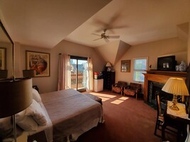 Een slaapkamer met een bed, een plafondventilator, een open haard en een balkon met gordijnen.