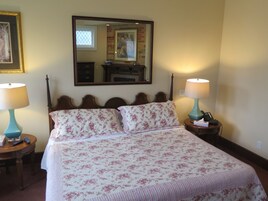 Een net opgemaakt bed met bloemenbeddengoed, twee bedlampjes, een spiegel boven het bed en een dressoir met spiegel.
