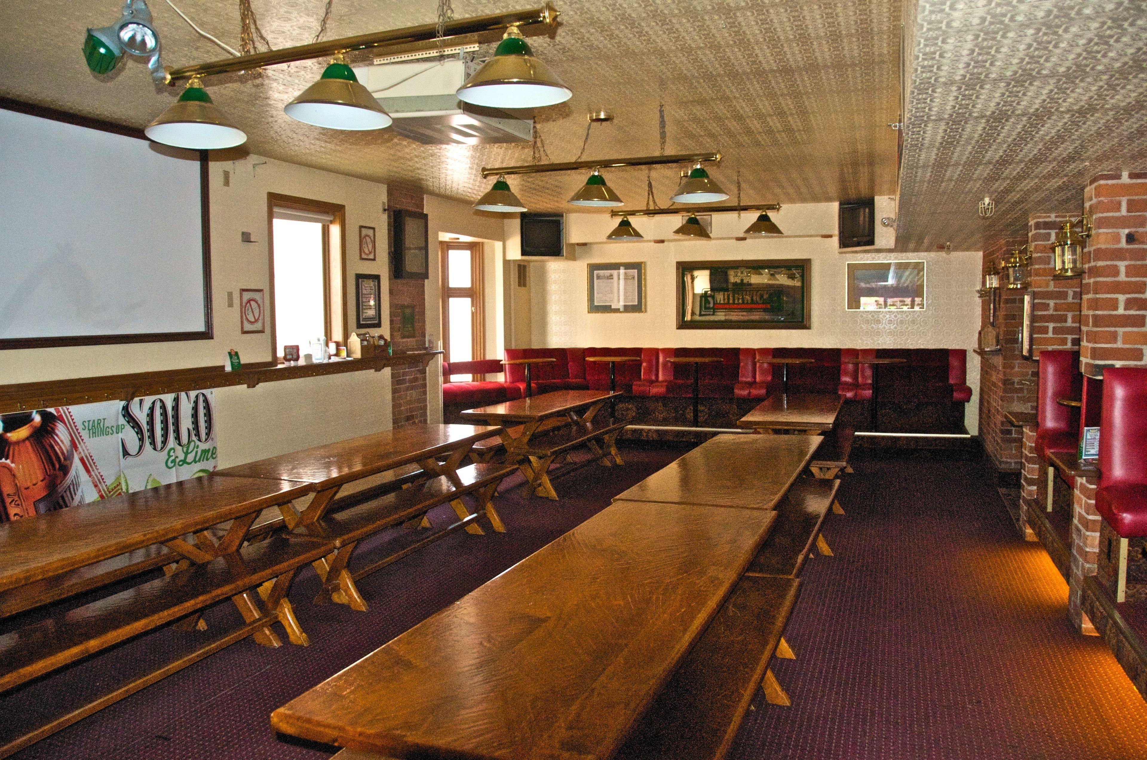 A restaurant with wooden tables and benches, brick walls, and hanging green lamps.