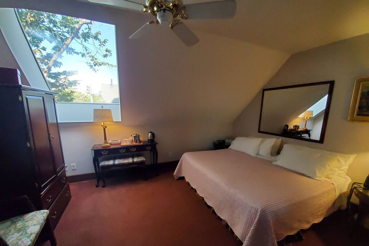 A bedroom with a bed, a desk with a lamp, a wardrobe, and a ceiling fan.