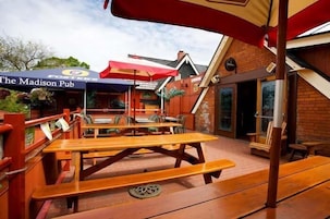 Un área de estar al aire libre con mesas de picnic de madera y sombrillas rojas en The Madison Pub.