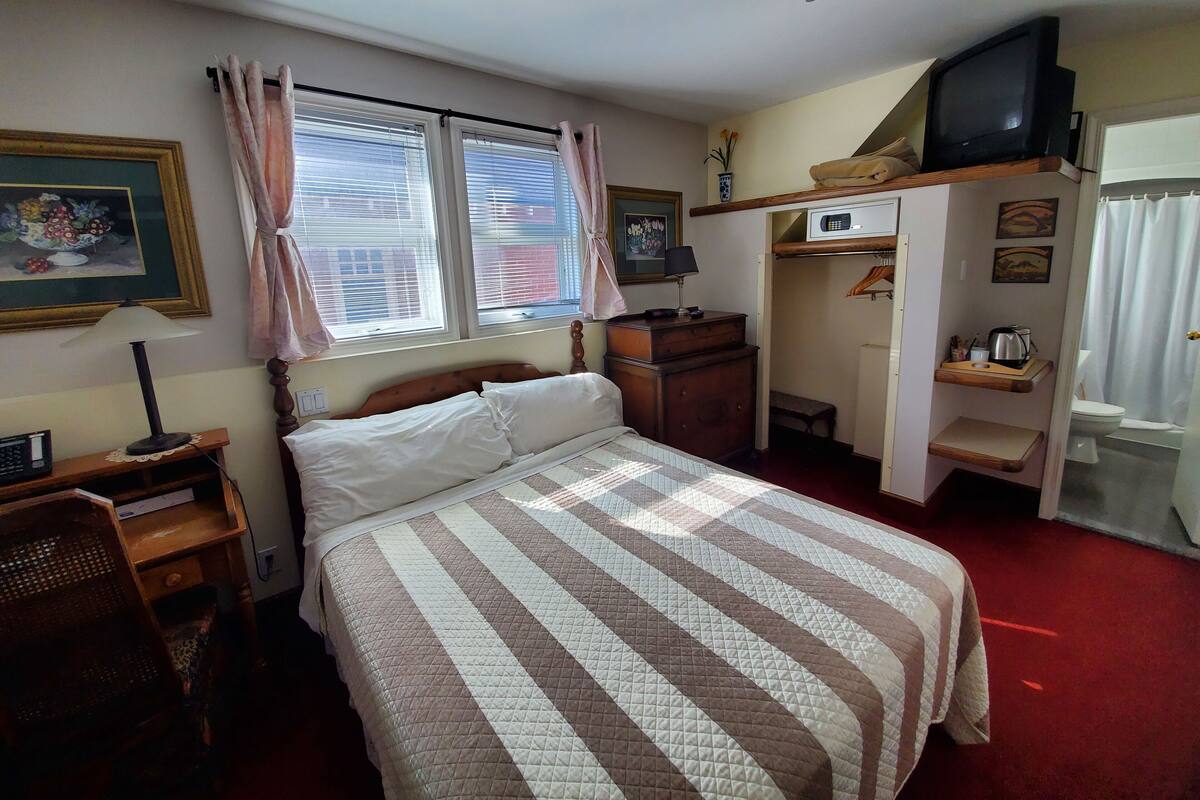 A neatly arranged bedroom with a bed, bedside table, lamp, and a TV on a shelf.
