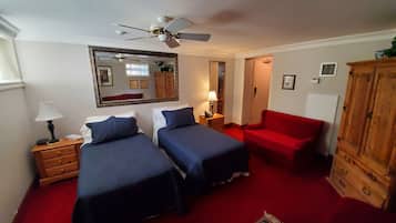A room with two beds, a red sofa, a wooden cabinet, a ceiling fan, and a mirror on the wall.