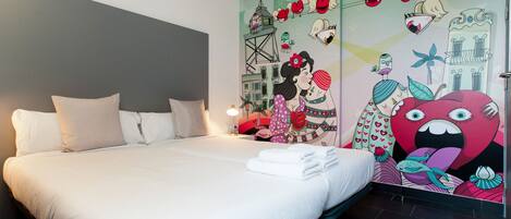 Quarto de hotel com uma cama grande, roupa de cama branca e um mural colorido na parede.