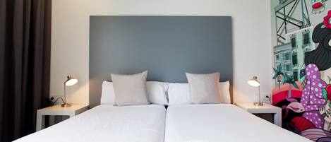 A double bed with white linens and two bedside tables with lamps.