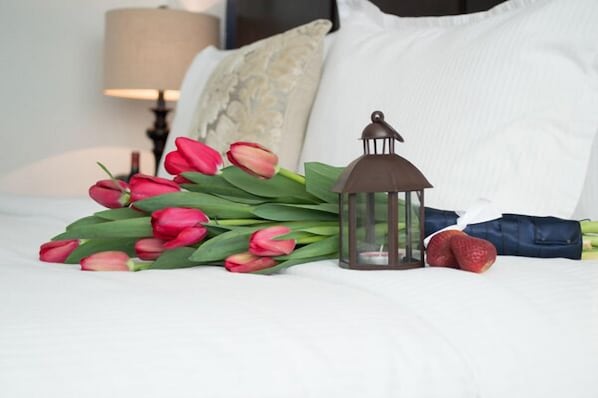 A bed with white bedding, a bouquet of red tulips, a lantern, and a strawberry.
