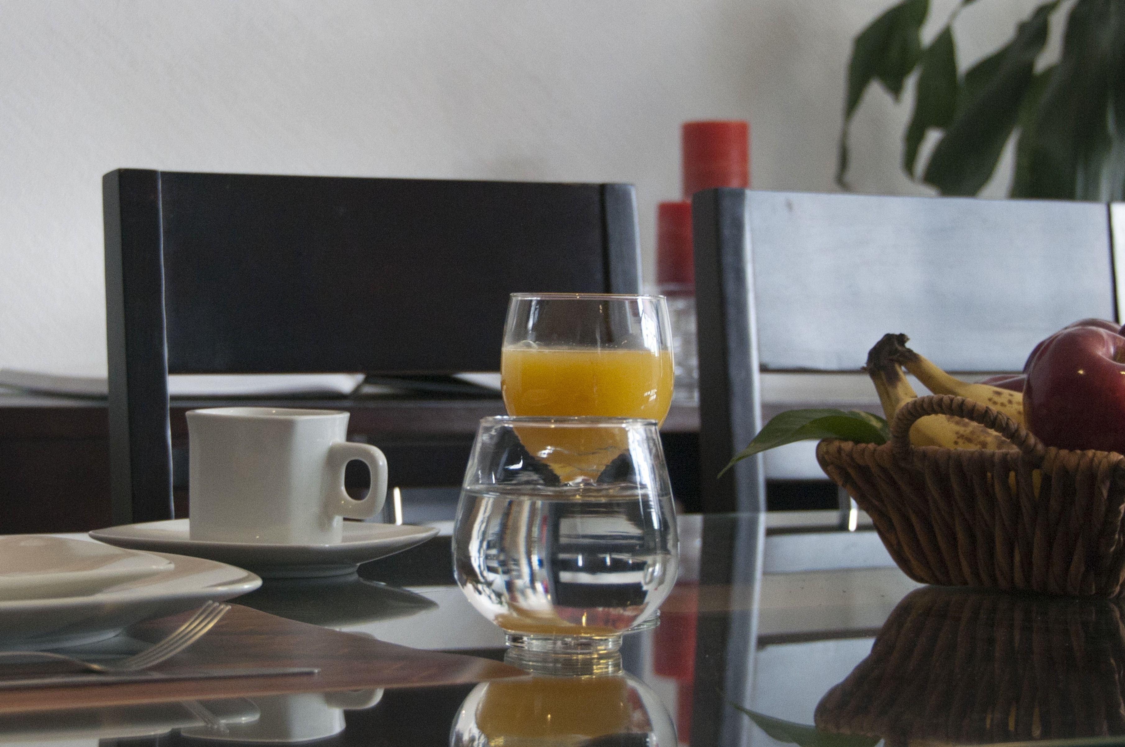 Ein Frühstückstisch mit einem Glas Orangensaft, einer Tasse und einem Obstkorb.