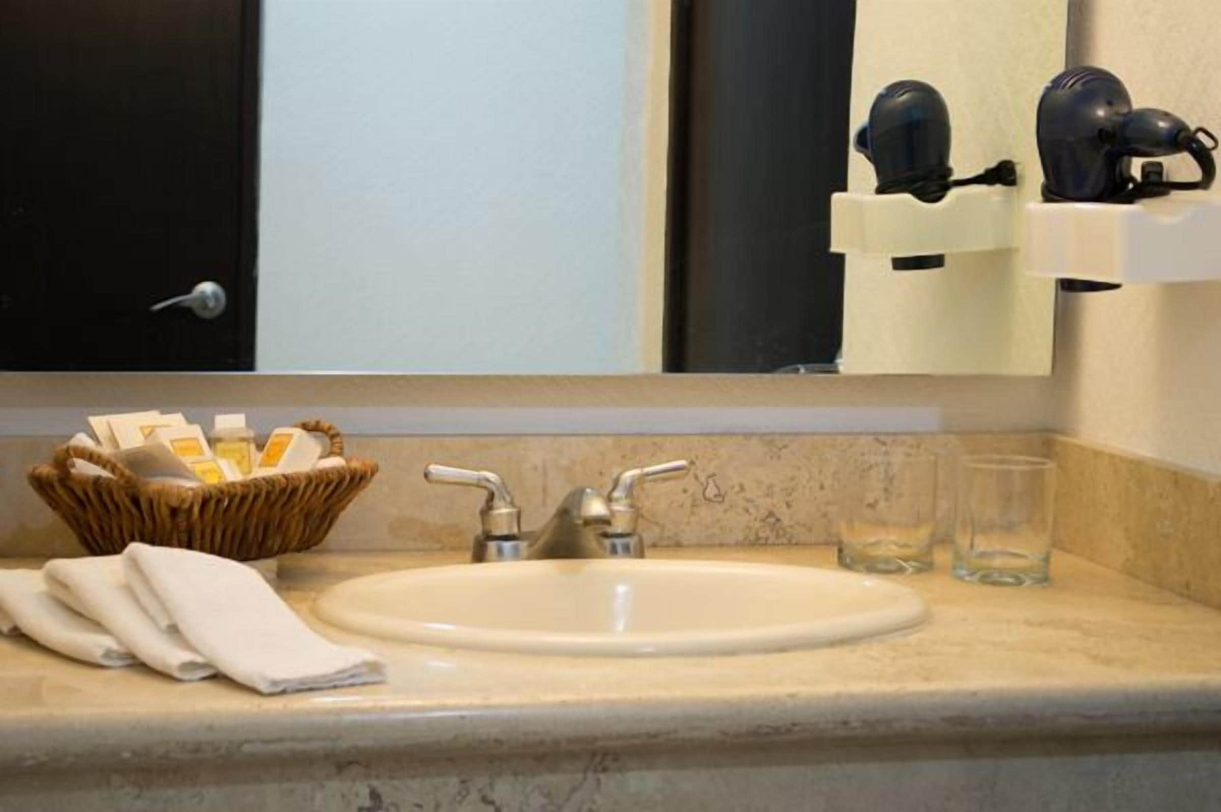 Une salle de bain équipée d’un lavabo, d’un miroir, d’un sèche-cheveux et d’un panier contenant des articles de toilette.