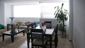 Ett vardagsrum med ett matbord, stolar, en soffa och en stor krukväxt.