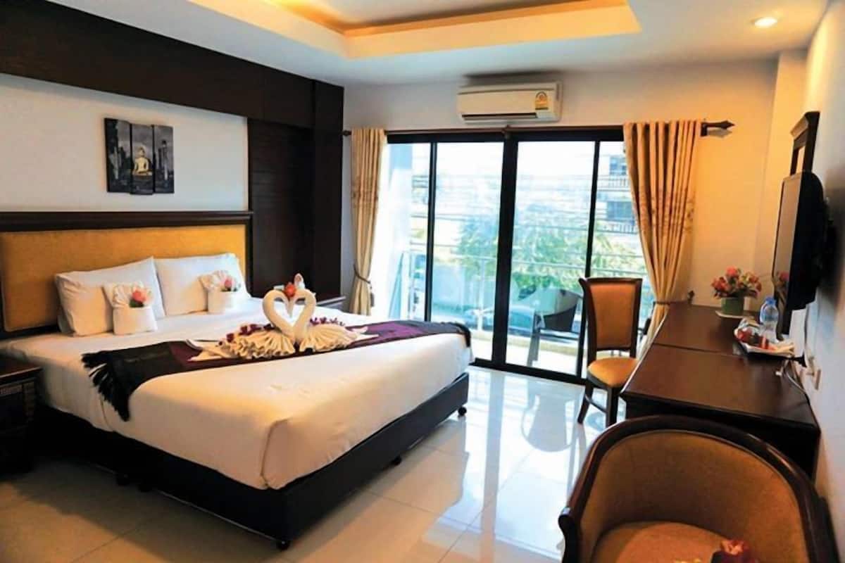 A hotel room with a large bed, a desk, a chair, and a view of the city through the window.