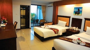 A hotel room with two beds, a dining table, and a balcony with chairs.