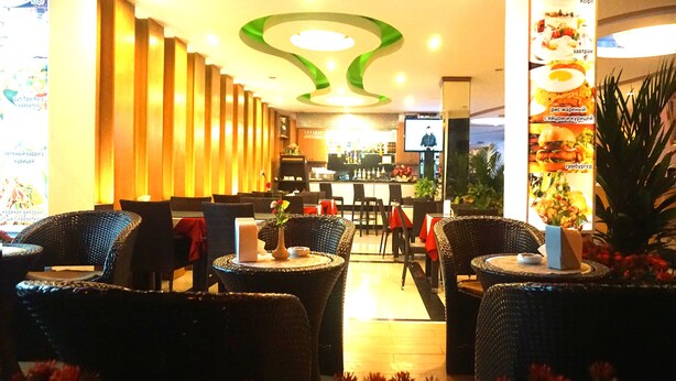 A restaurant with wicker chairs and tables, a bar area, and a ceiling with a green and white design.