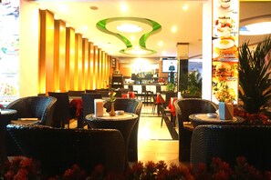 Een restaurant met rieten stoelen en tafels, een bar en een plafond met een groen-wit ontwerp.