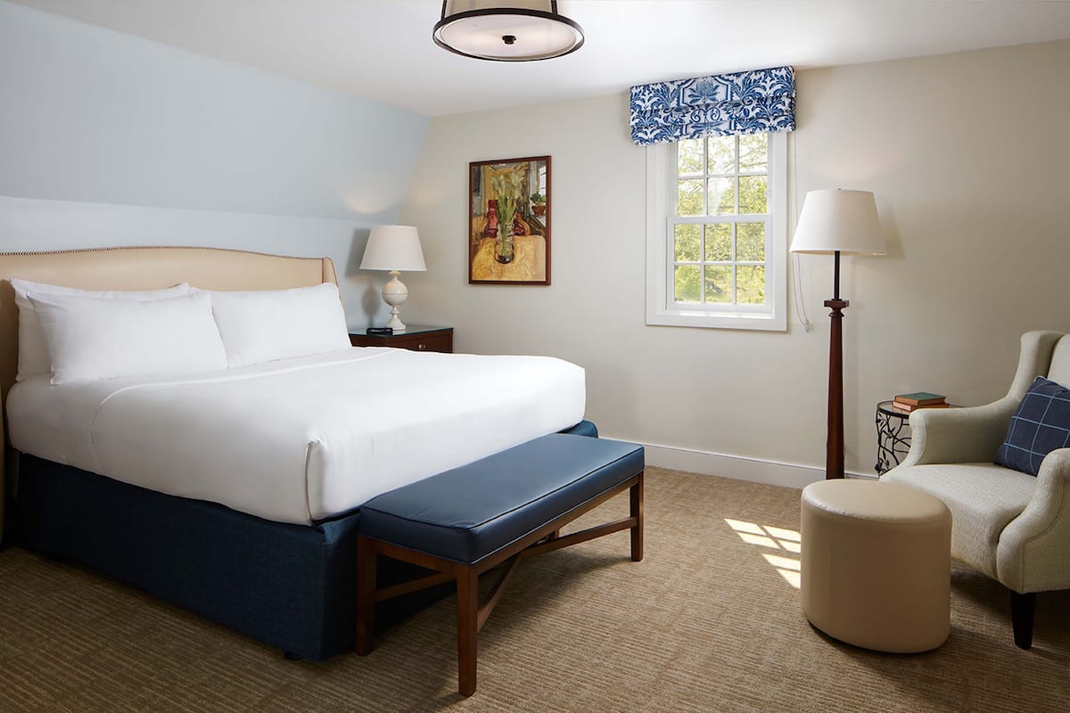 A neatly arranged hotel room with a large bed, a chair, a small table, and a window with curtains.