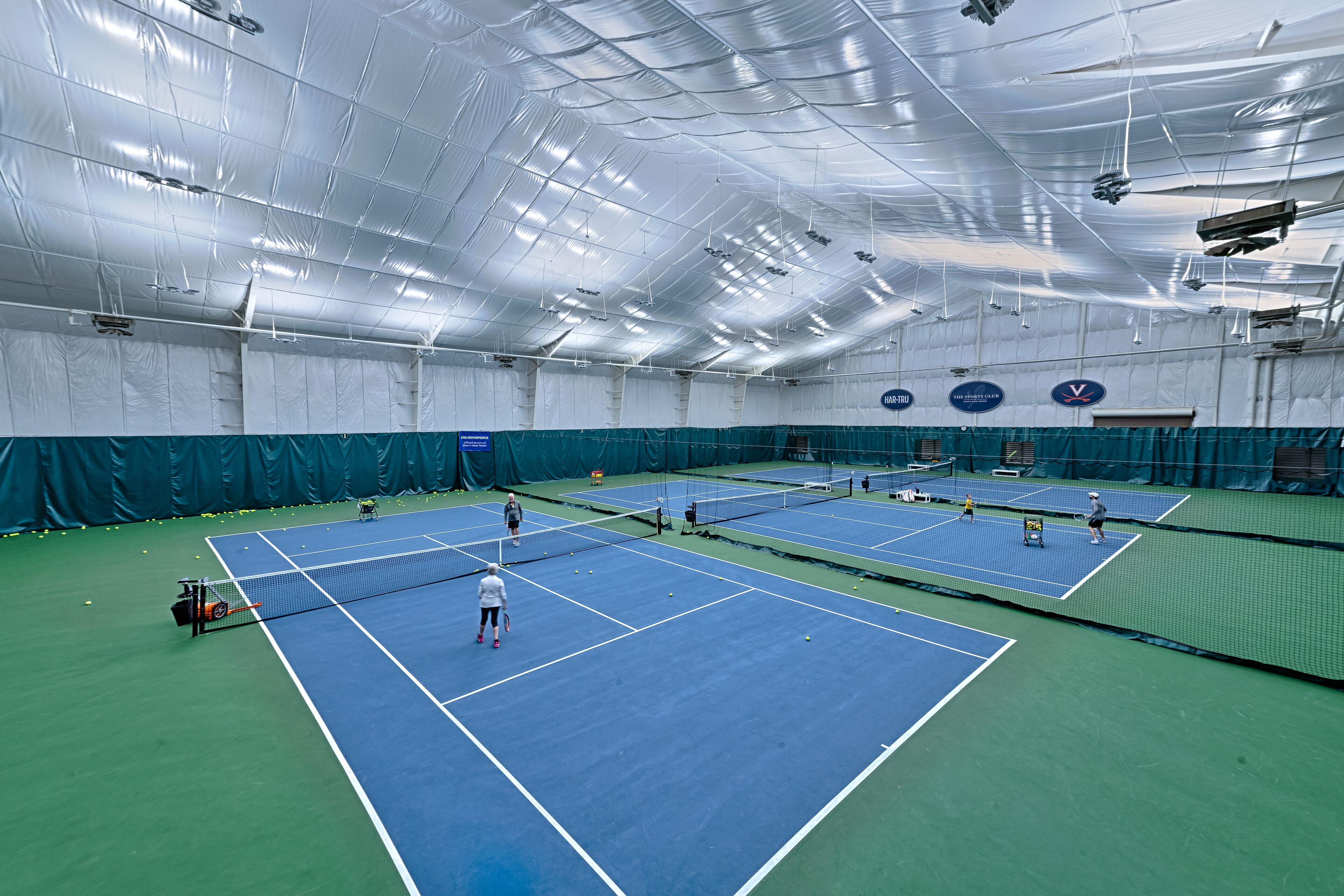 An indoor tennis facility with multiple courts, a net, and a ceiling with lights.