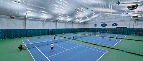 An indoor tennis facility with multiple courts, a net, and a ceiling with lights.